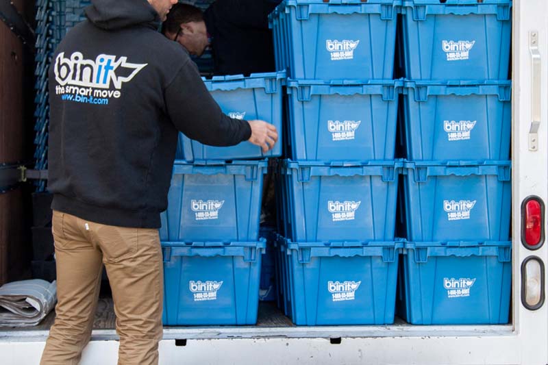 Bin It team member loading stacked blue bins into a moving truck