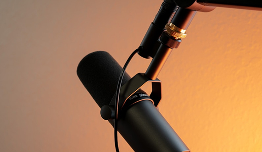 Close-up of a black microphone with a foam windscreen against an orange gradient background.