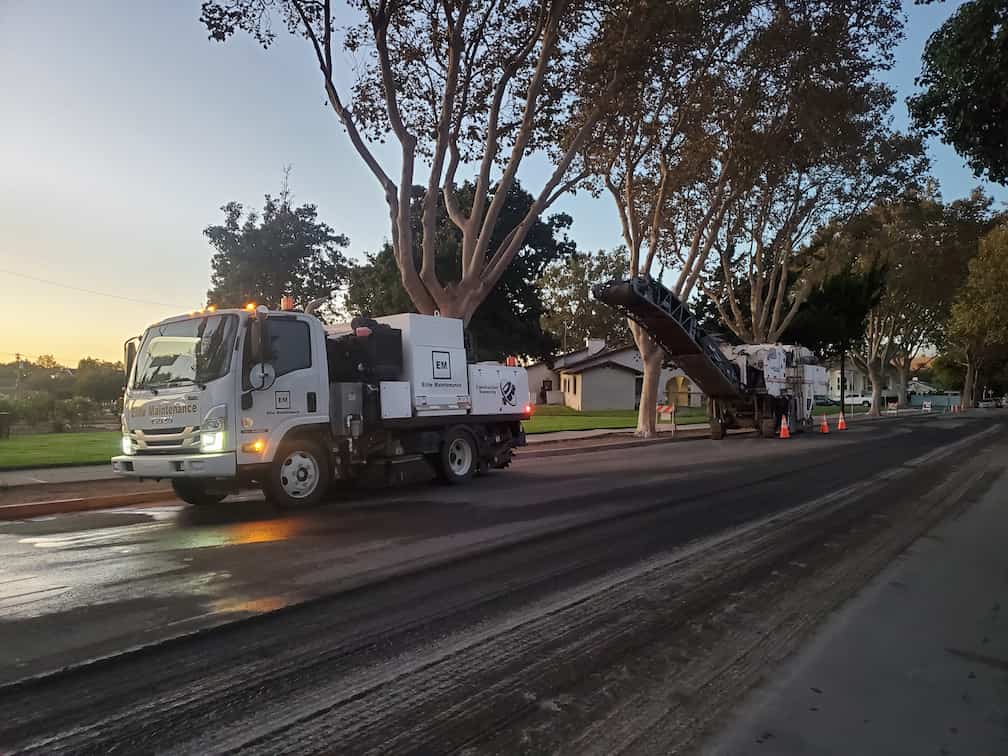 Contractor sweeping asphalt millings alongside paving crew