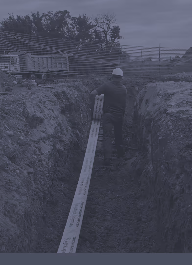 Construction worker in a hard hat installing Signaltape® Underground Warning Tape in a trench.
