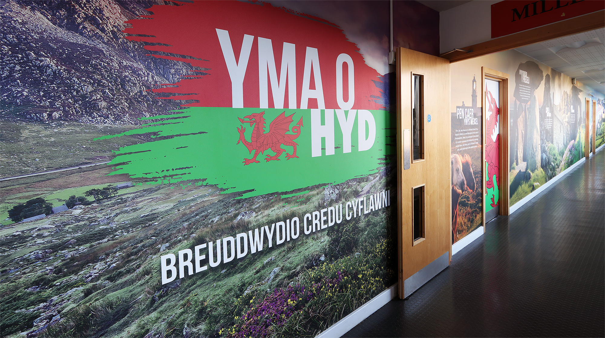 This striking wall art proudly displays the bold statement "Yma o Hyd," meaning "Still Here" in English. It celebrates the resilience of the Welsh language and its importance in school life at Ysgol Greenhill. Wall art like this not only honors heritage but inspires pride and connection - Every school should have spaces that tell their unique story!