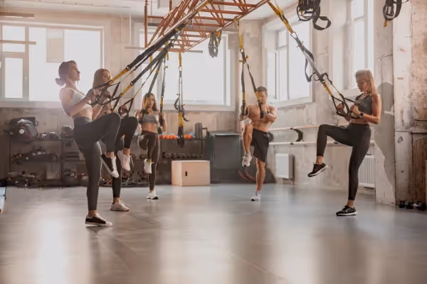  An image of a group of individuals engaged in suspension training exercises in a well-equipped, modern gym.