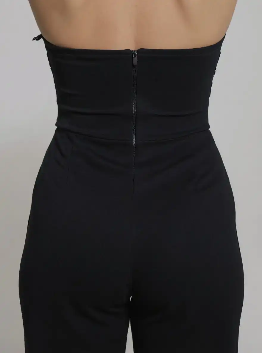 Enterizo strapless en punto compacto negro, con bustier fruncido y aplique floral en el centro. Talle alto marcado y pernera recta y larga que alarga la figura. Cierre trasero invisible para un acabado limpio y elegante.