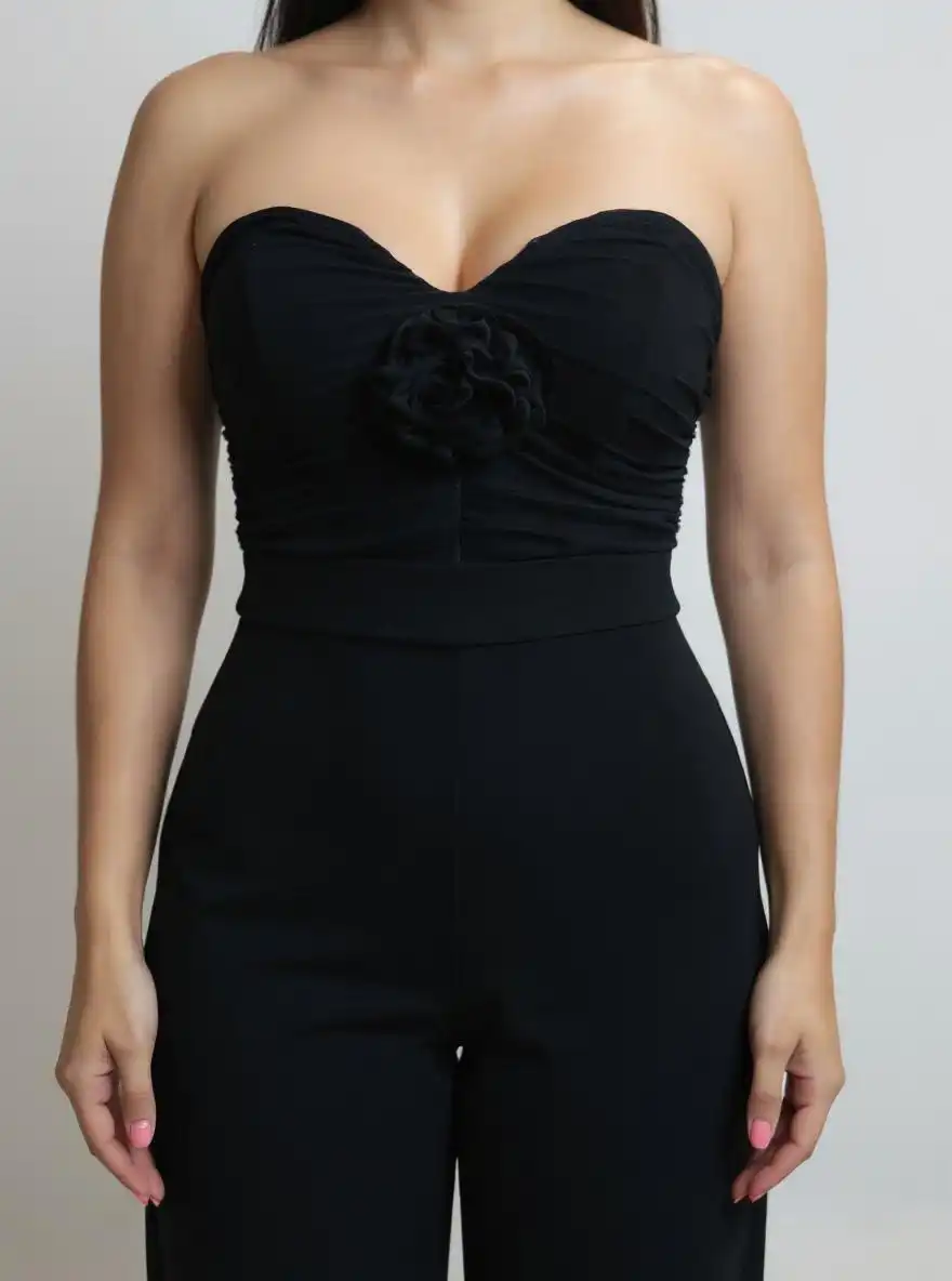Enterizo strapless en punto compacto negro, con bustier fruncido y aplique floral en el centro. Talle alto marcado y pernera recta y larga que alarga la figura. Cierre trasero invisible para un acabado limpio y elegante.
