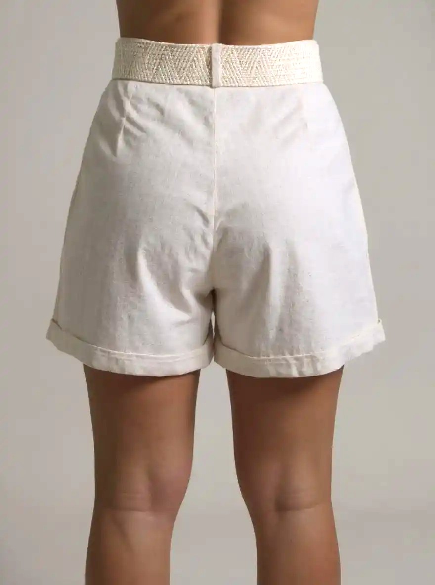 Short de lino en tono crudo con cinturón tejido removible en color beige con hebilla redonda decorativa. Presenta pretina con pasadores, dobladillo en botas y cierre delantero oculto. Ideal para looks casuales de clima cálido.