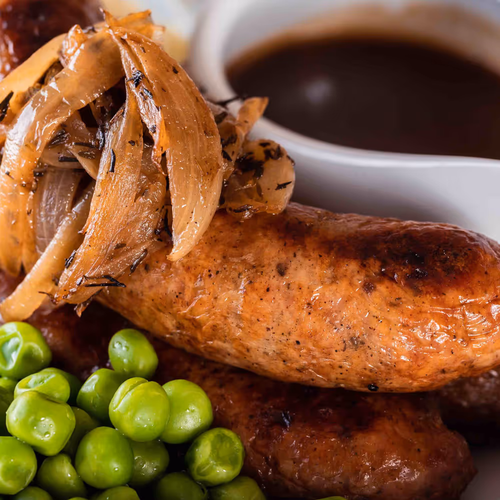 Grilled sausages topped with caramelized onions, served with green peas and brown gravy sauce.