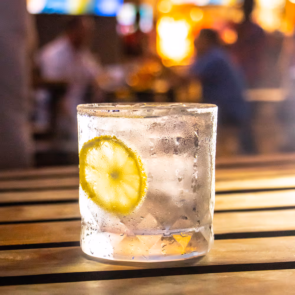 Cold glass of water with ice and a lemon slice on a wooden table in a dimly lit setting.