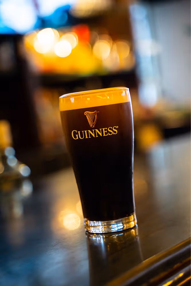 Glass of dark Guinness beer with creamy foam on a reflective bar counter.