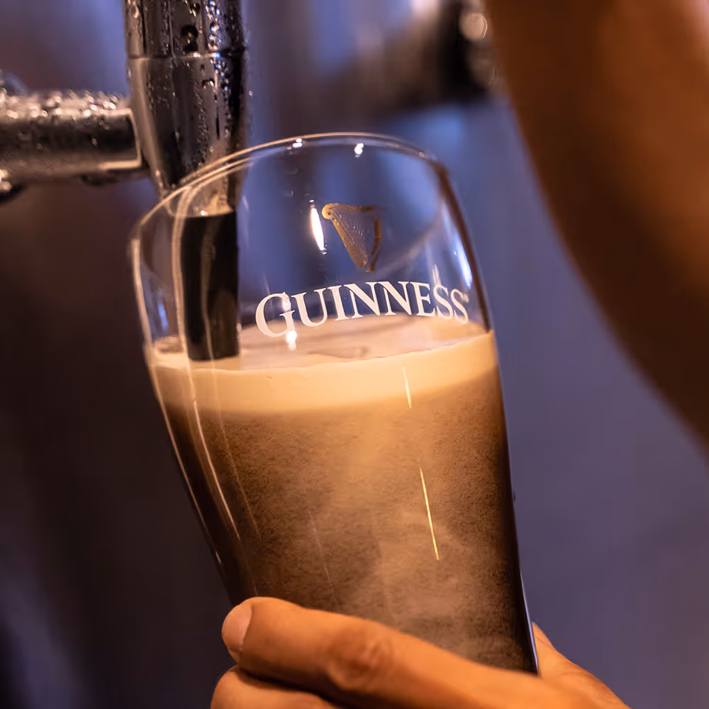 Close-up of a hand holding a Guinness glass being filled with dark beer from a tap.