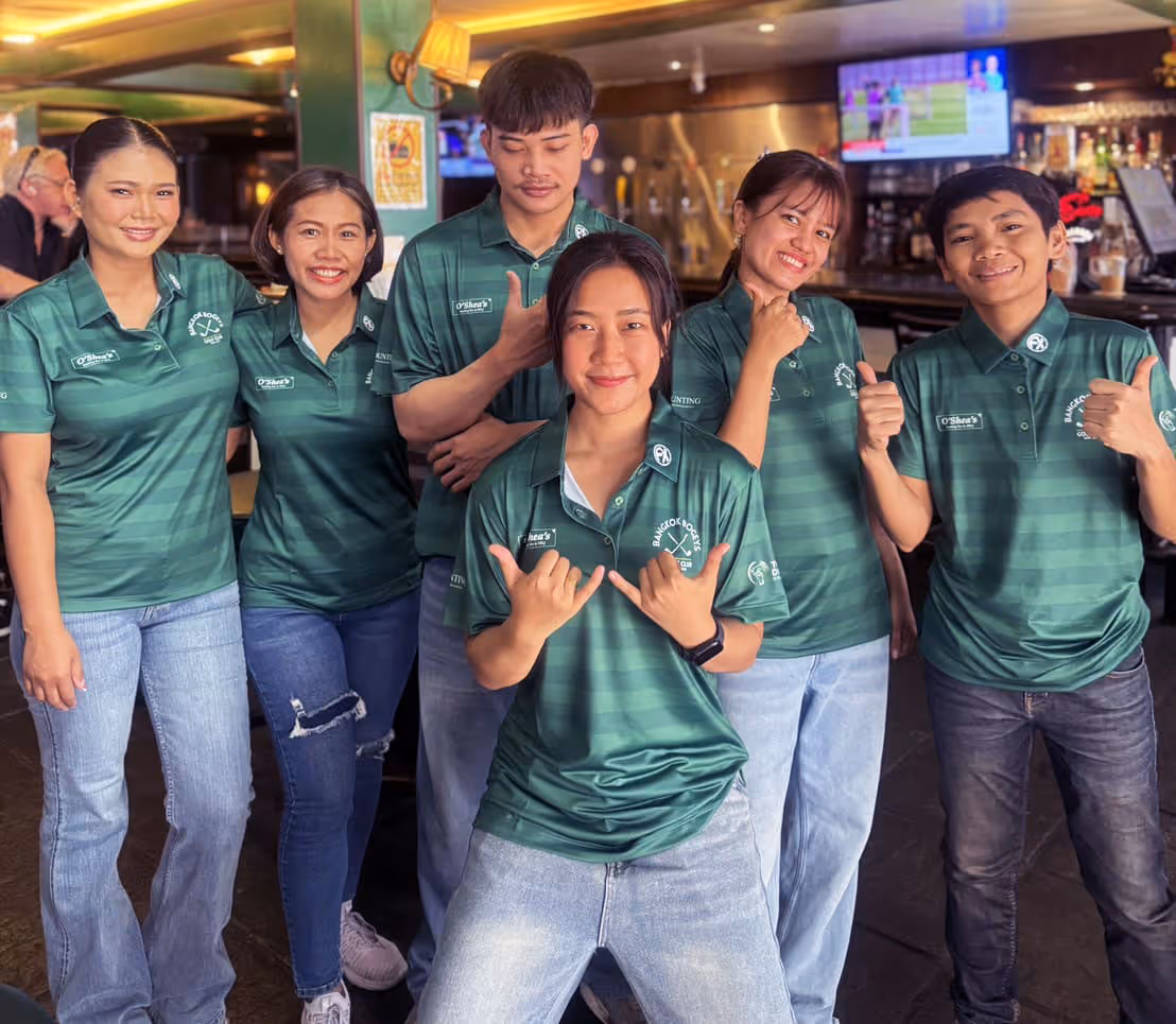 Six smiling people wearing matching green polo shirts posing inside a bar or restaurant.