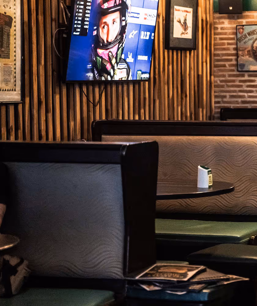 Empty restaurant booths with a television showing a helmeted racecar driver on a wooden slat wall.