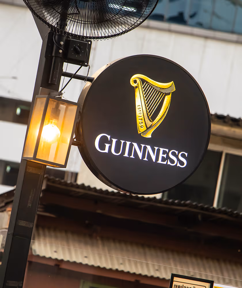 Round Guinness pub sign with golden harp logo and illuminated street lamp on metal pole.