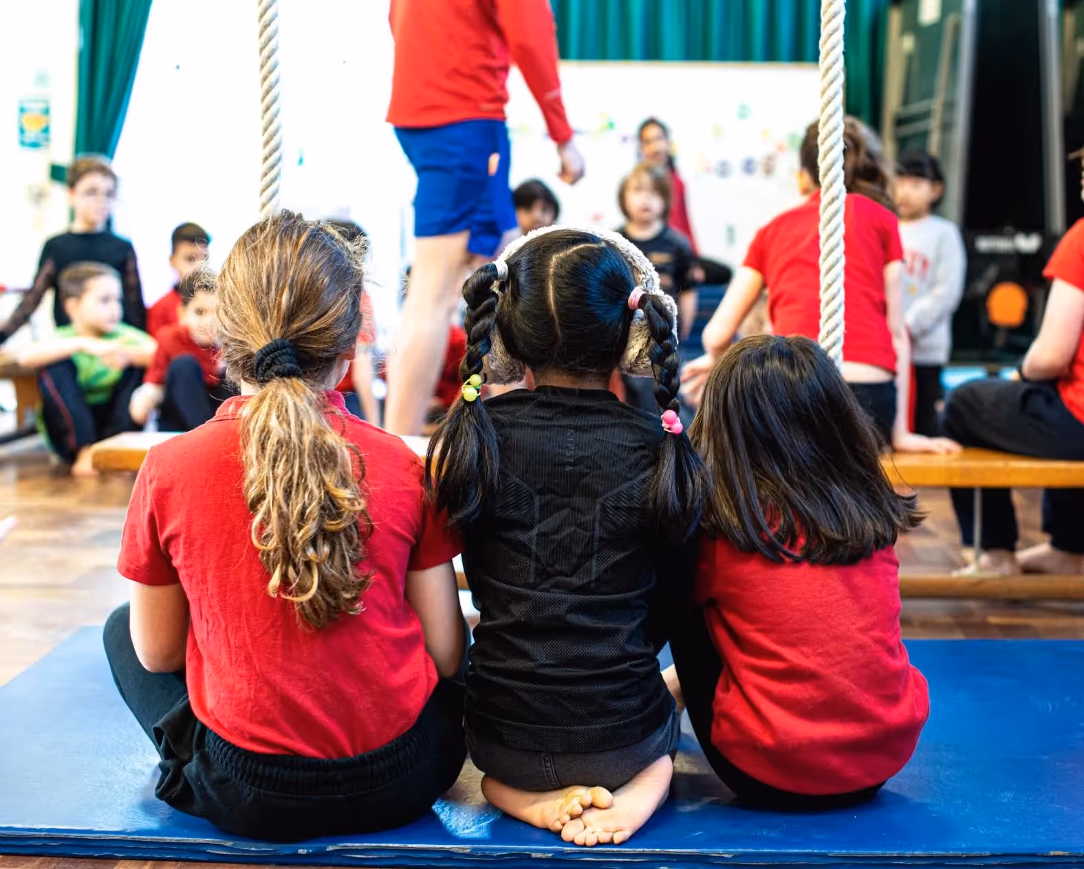 An assembly hall full of primary school children listening to a teacher.