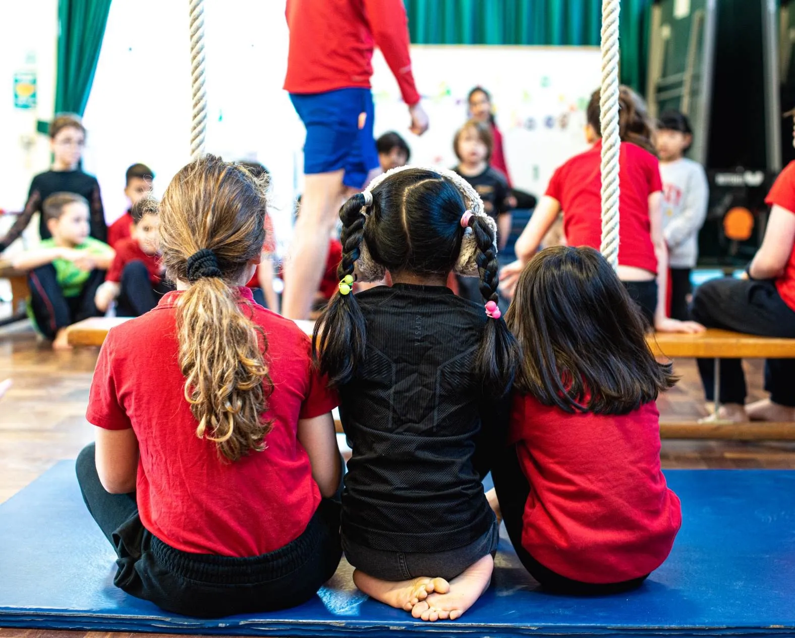 An assembly hall full of primary school children listening to a teacher.