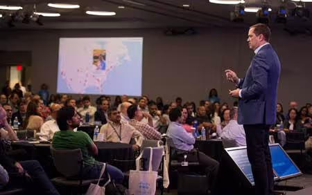 Corporate Cisco event. The photo shows a speaker and Cisco's employees and a screen showing a social media wall with the maps theme, showing posts from all over the world