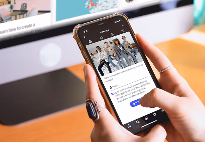 Photo of a person holding a smartphone and posting content on Instagram, with a Walls.io social wall visible on a computer screen in the background.