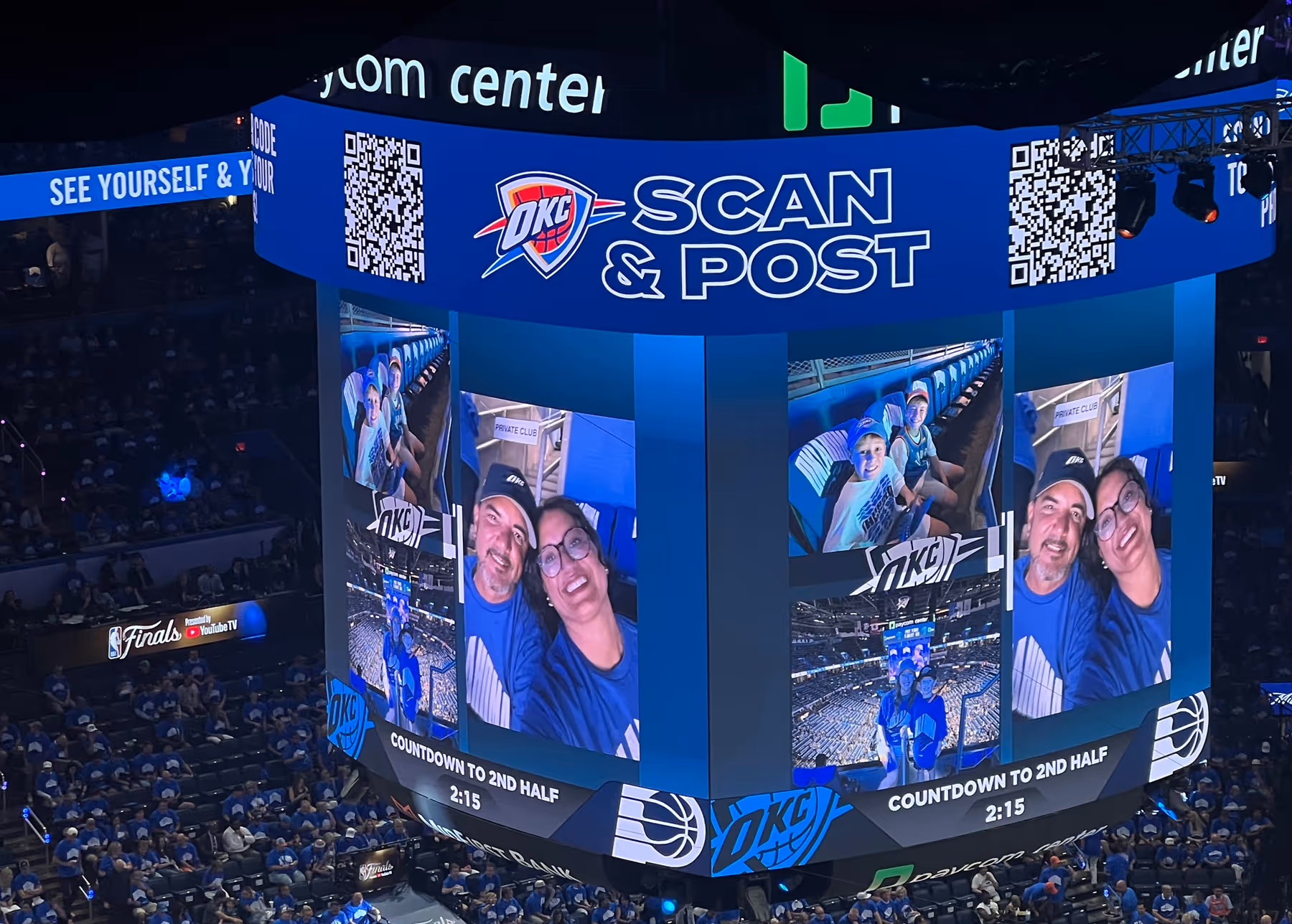 A large arena screen at an Oklahoma City Thunder basketball game displays fan photos shared through a “Scan & Post” campaign. The jumbotron shows smiling attendees in team shirts, with a countdown to the second half at the bottom. The stands are filled with fans wearing blue.