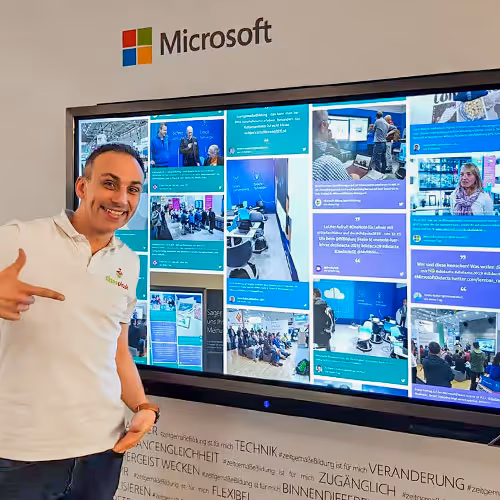 A Microsoft social media wall displaying brand content on a screen. An employee pointing toward it.