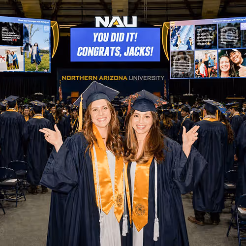 A photo of two students posing at a graduation party with social media screens full of user-generated content behind them at a nau graduation 