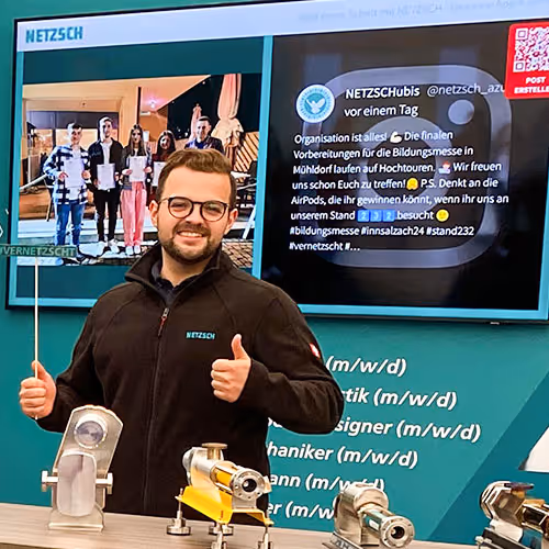 The photo of a man posing with props at a trade show booth with a social media display behind of him