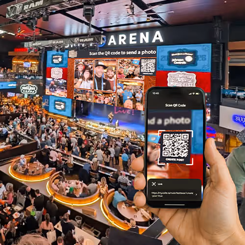 A concert stage with a social wall full of fan content at the Texas Music Festival. A venue full of people and a hand with a phone scanning the QR code on the social wall to submit a photo.
