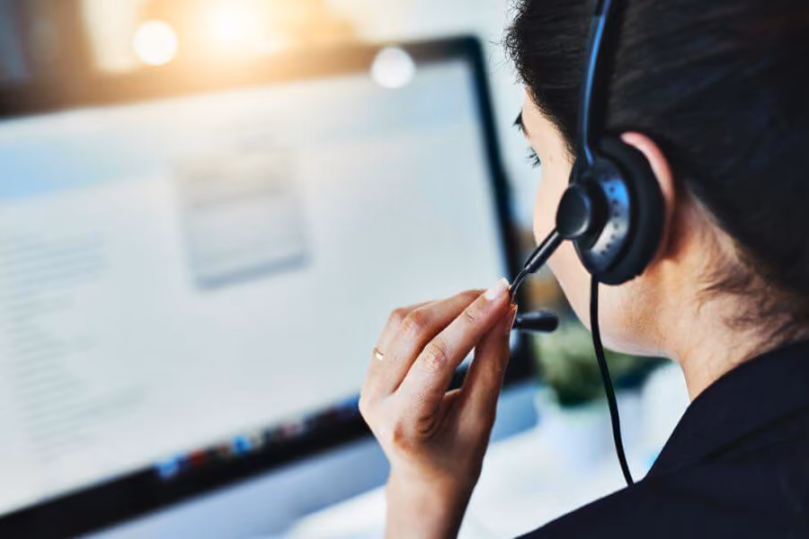 A support agent wearing a headset works at a computer, seen from behind.