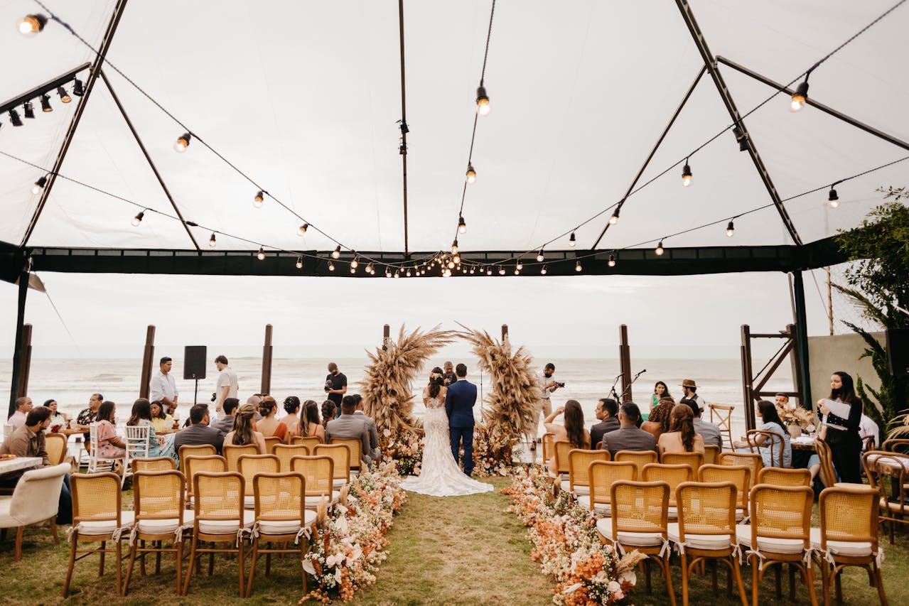 A beachside wedding ceremony under a white tent with string lights