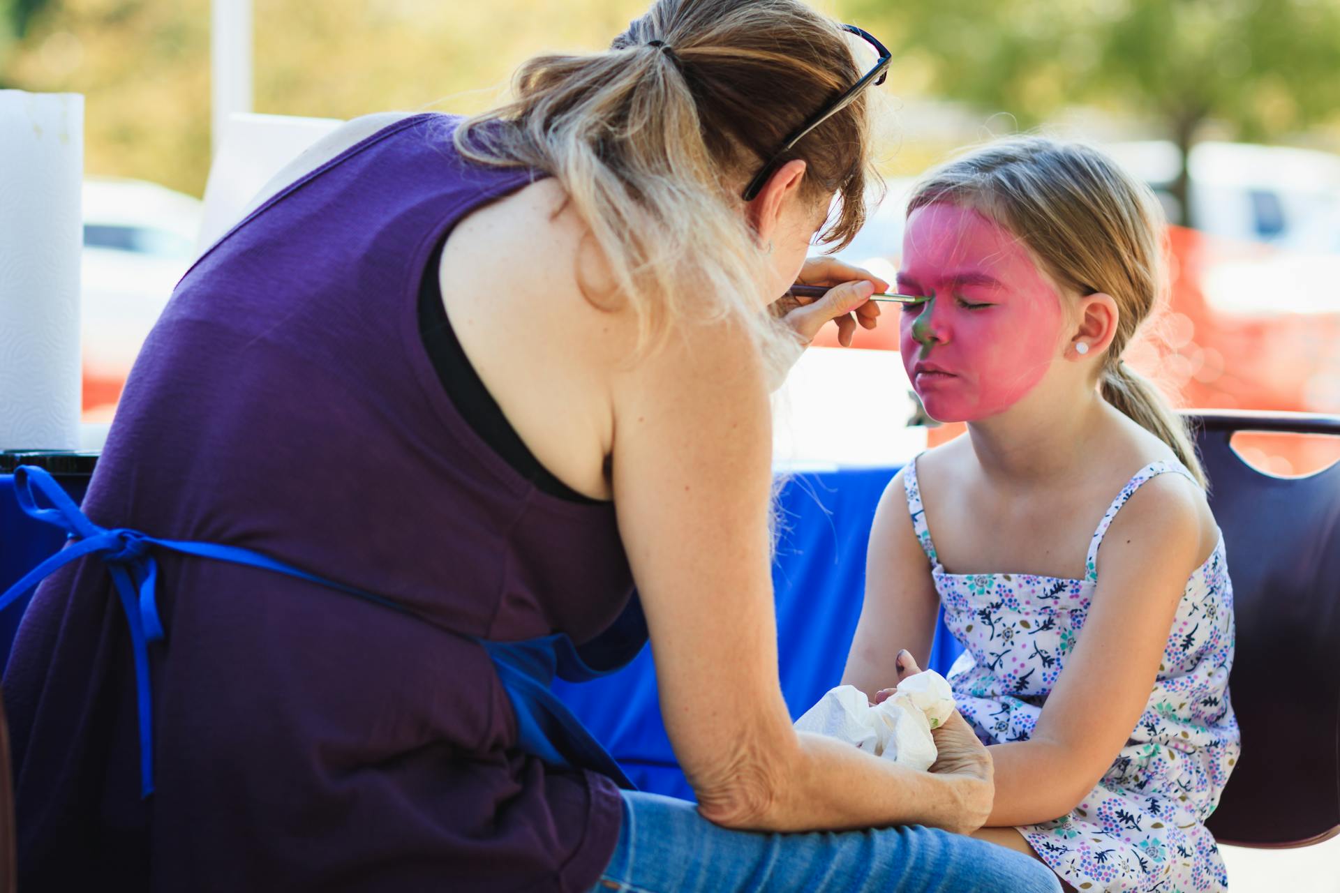 Young girl getting her face painted by a woman