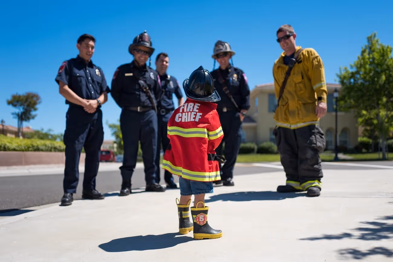 Photo of a young child in a Fire Chief outfit surrounded by adult firemen