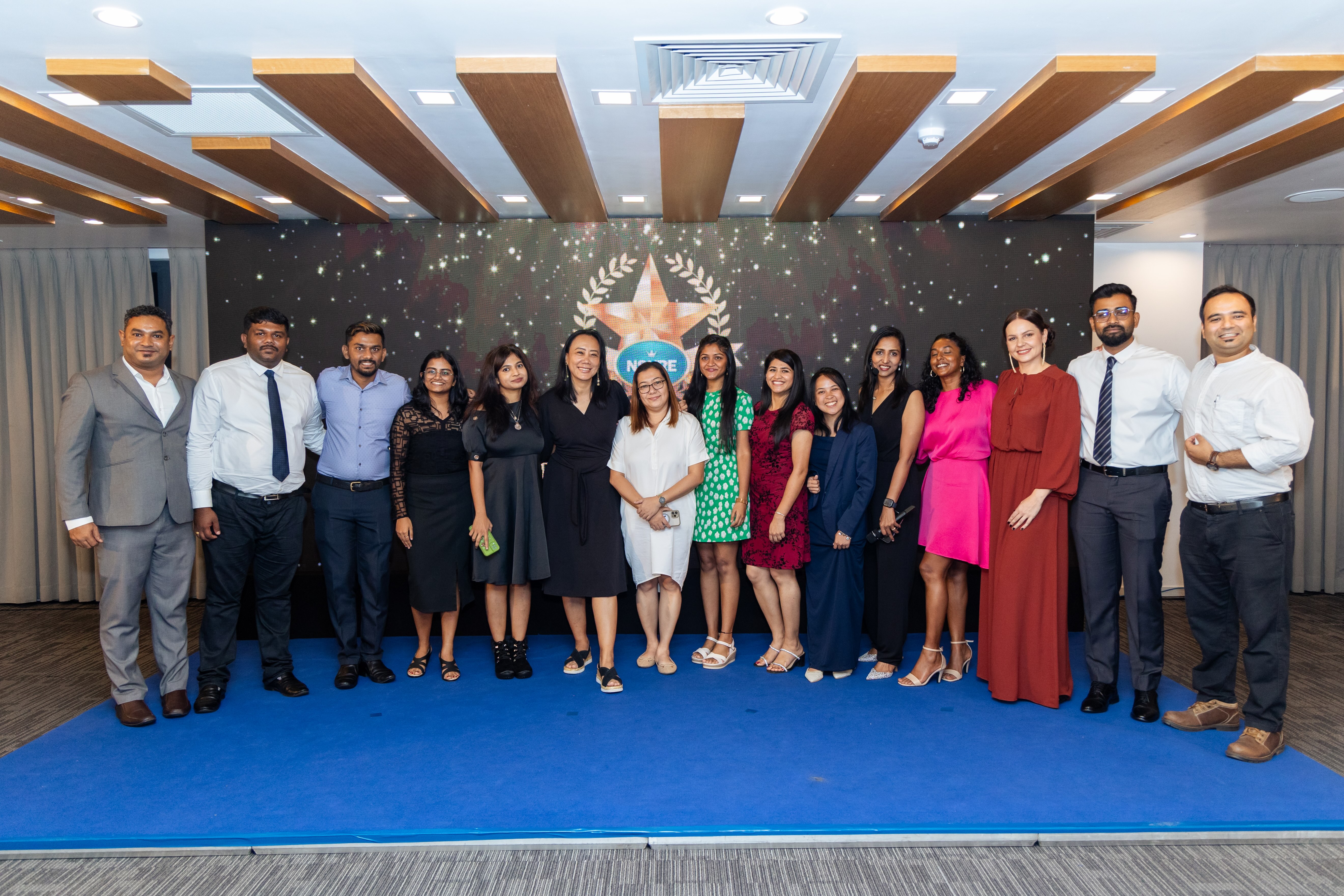 Group of 15 people, the Nsure team, posing indoors on a blue carpet with a star-themed backdrop.