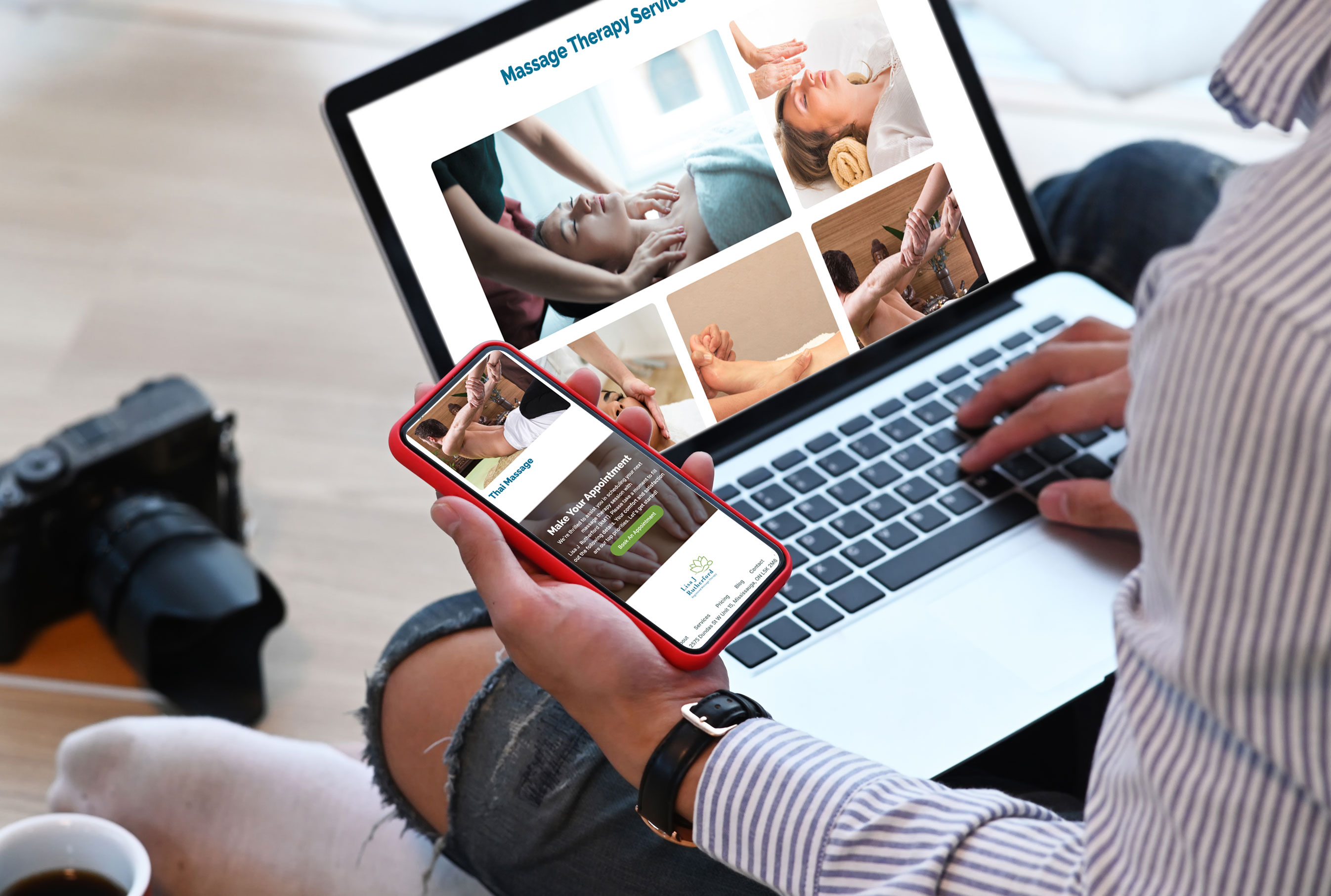 Person sitting cross-legged using both a smartphone and a laptop to view Lisa J Rutherford Massage Therapy's website. The laptop screen displays various massage therapy services with images, while the phone shows the Thai Massage service page and an appointment booking section. A camera, coffee cup, and notebook are placed nearby, emphasizing a casual, creative setting.