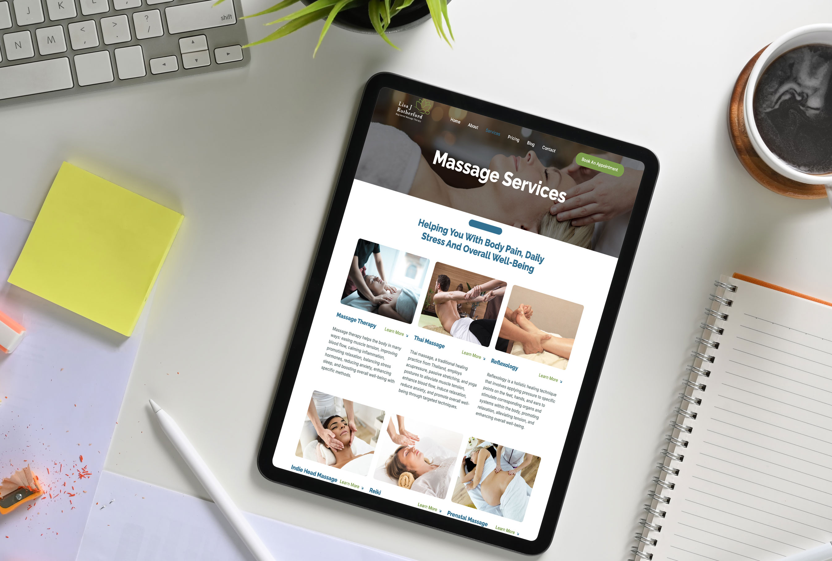 Tablet on a white desk displaying the 'Massage Services' page of Lisa J Rutherford Massage Therapy's website. The screen shows various massage options including Thai Massage, Reflexology, Indie Head Massage, Reiki, and Prenatal Massage, with corresponding images and brief descriptions. Surrounding the tablet are office supplies, a cup of coffee, a notepad, sticky notes, a pencil, and a plant, creating a productive workspace vibe.