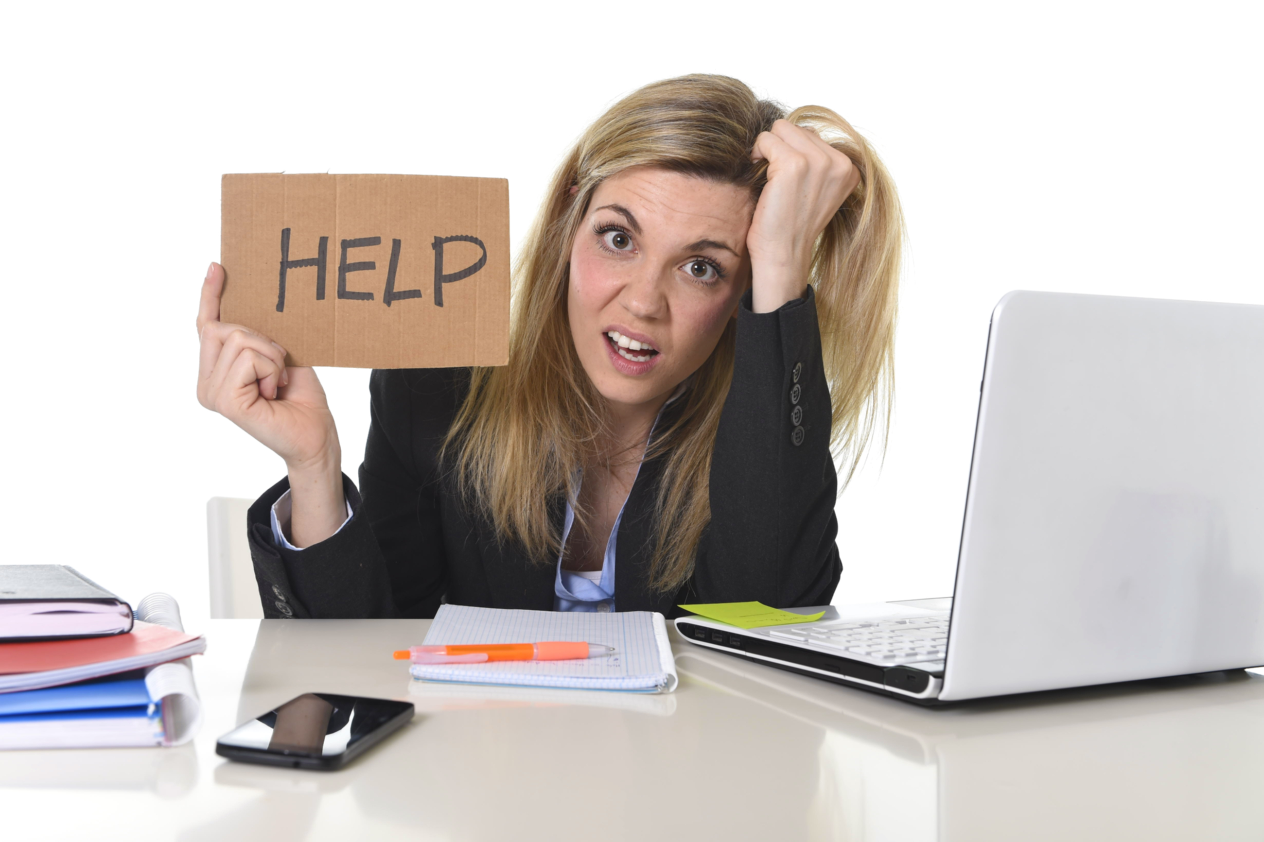 Overwhelmed professional at a desk holding a help sign, illustrating business frustration caused by unclear strategy, scattered tools, and lack of direction.