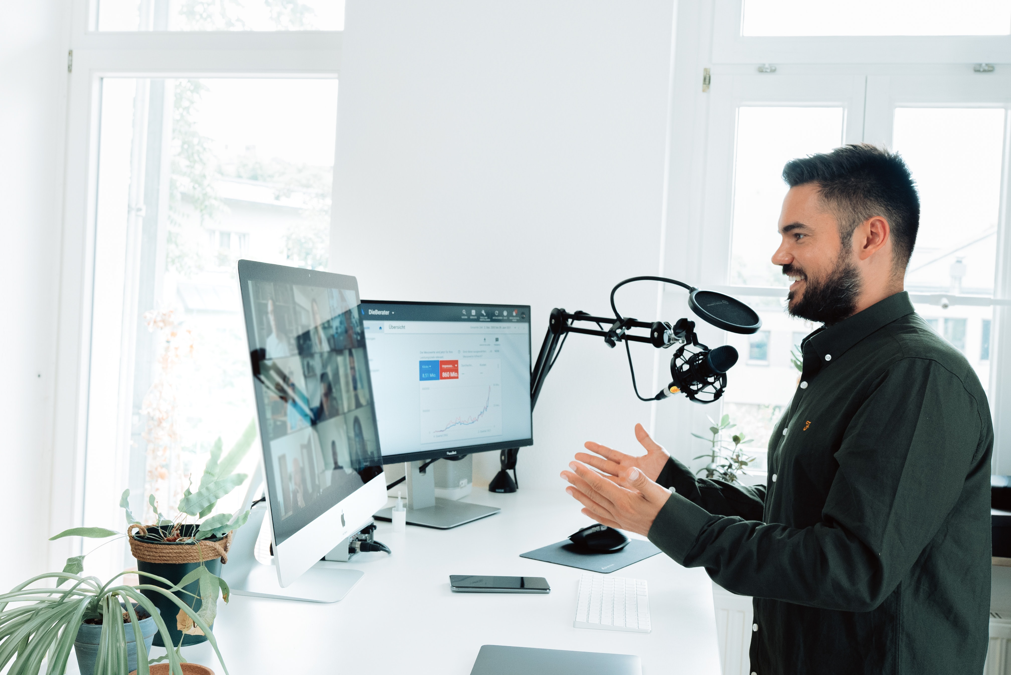 A man standing by his desk, having a video-conference, and speaking into a microphone
