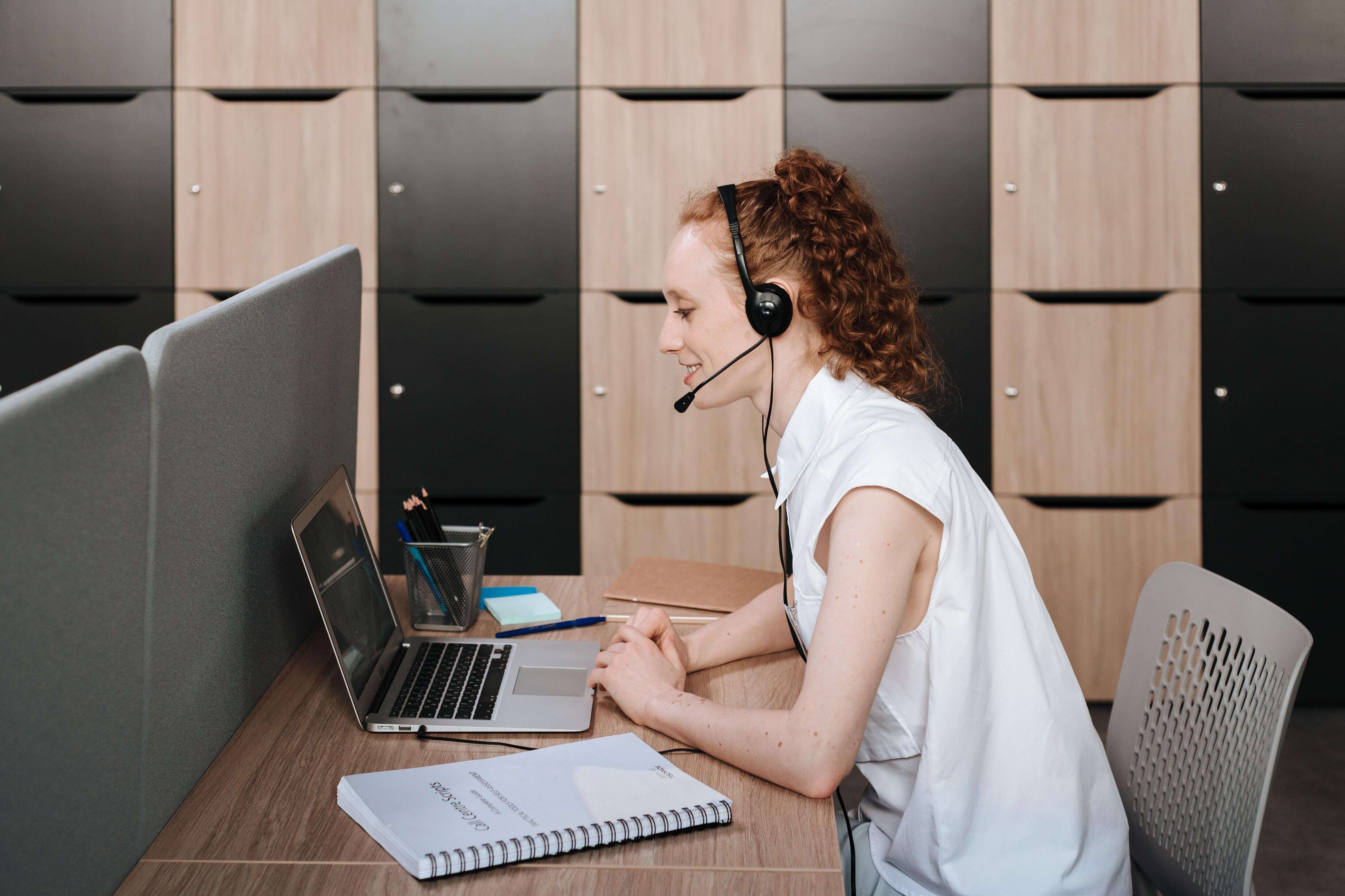 A woman with a headset talking to someone on her computer