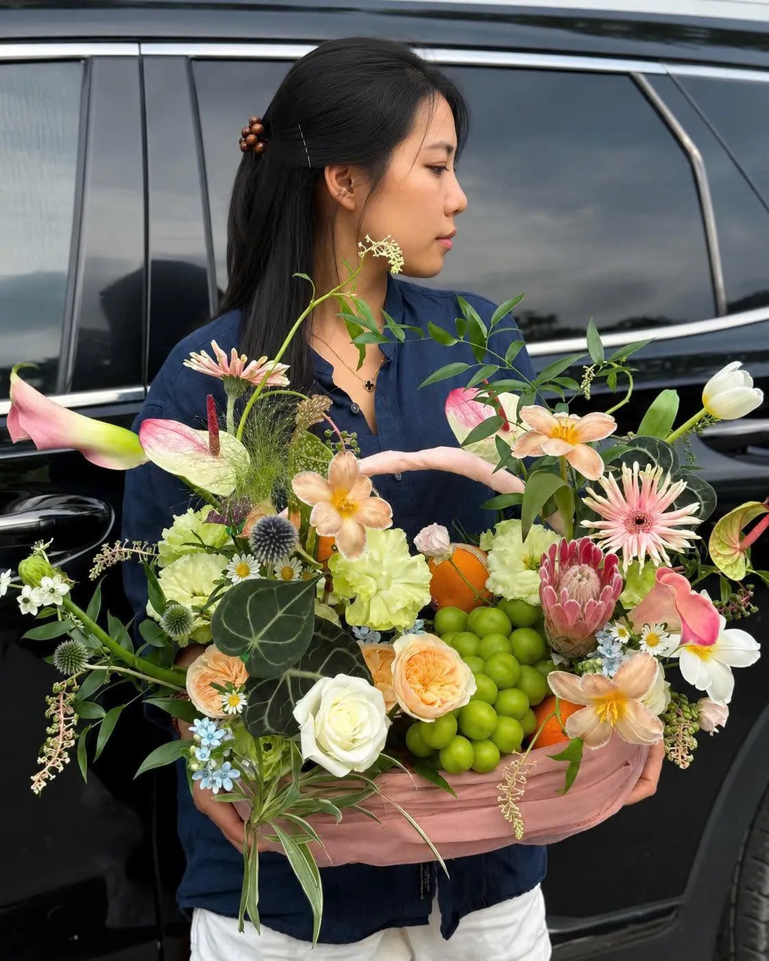Cô gái bưng giỏ hoa nghệ thuật phối trái cây cạnh xe tại Huyện Cư Jút, Đăk Nông