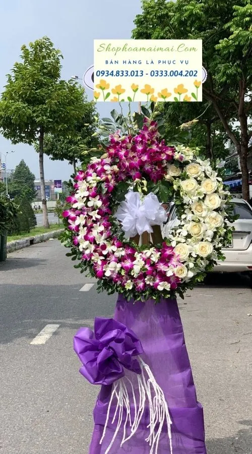 Màu sắc: của sản phẩm là tím phối trắng. Dịp tặng: lễ viếng, lễ tang, lễ nhập quan, tiễn biệt, chia buồn. Loại sản phẩm: Hoa chia buồn / hoa tang lễ.

Cõi Vĩnh Hằng - HCB.04 được Hoa Mãi Mãi giới thiệu như một mẫu vòng hoa lớn phúng điếu tinh tế, gói trọn sự trang nghiêm và lòng thành kính, thích hợp cho lễ nhập quan, lễ viếng và lễ di quan.

Tone màu chủ đạo của sản phẩm là tím phối trắng, được phối hợp hài hòa để toát lên vẻ trang nghiêm, thanh khiết, phù hợp với không khí lặng lẽ, tiếc thương của tang lễ.

Điểm nhấn của sản phẩm là lan mokara tím và hồng trắng, kết hợp cùng lá cau, nơ tím trắng tạo chiều sâu và sự hài hòa cho tổng thể, giúp thành phẩm trông đầy đặn, tinh tế mà không rườm rà.

Sản phẩm cao khoảng 1,6 – 1,7m, đường kính phần hoa chính 60 – 70cm khi hoàn thiện, đủ để tạo điểm nhấn trang trọng trong không gian lễ viếng; kích thước có thể thay đổi theo yêu cầu cụ thể của quý khách.

Thông điệp gửi viếng: đi kèm bảng tên trang trọng thể hiện rõ mối quan hệ và lời tiễn biệt, nội dung có thể là "Kính viếng", "Thành kính phân ưu" hoặc lời nhắn riêng do quý khách cung cấp.

Tùy biến mẫu theo yêu cầu: Ngoài mẫu tiêu chuẩn, quý khách hoàn toàn có thể yêu cầu thay đổi tông màu, loại hoa hoặc kích thước cho phù hợp với hoàn cảnh cụ thể; Hoa Mãi Mãi cam kết hoa luôn tươi mới và giao hàng tận nơi đúng hẹn.