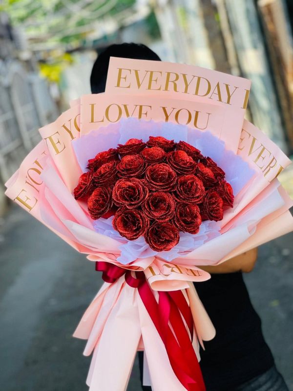 Màu sắc: đỏ đô ánh nhũ. Dịp tặng: tỏ tình, Valentine, kỷ niệm, sinh nhật người yêu. Loại sản phẩm: Hoa sáp.

Bó Hoa Sáp Tỏ Tình dùng hồng sáp đỏ đô phủ nhũ kim tuyến, bắt sáng lấp lánh rõ rệt, đặt trên nền giấy hồng phấn in chữ nhũ vàng "Everyday I Love You" lặp lại. Cặp màu đỏ đô và hồng phấn làm bó vừa nổi vừa mềm mại.

Bó gồm khoảng 30 đến 40 bông hồng sáp kết thành mặt vòm, không pha lá nên khối màu liền mạch.

Phần giấy phía sau xếp nhiều lớp dựng cao như hình quạt, lớp lót trong bằng giấy pelure trắng pha tím nhạt, thắt nơ ruy băng satin đỏ đô thả dài. Bó cao khoảng 50 đến 55cm, bề ngang phần giấy chừng 35 đến 40cm, trông cao ráo khi cầm đứng.

Mẫu này hợp với buổi tỏ tình, lễ Valentine, kỷ niệm ngày quen nhau hoặc sinh nhật người yêu, dành tặng bạn gái, người yêu hoặc vợ, nhất là khi anh muốn một bó nhìn lấp lánh trong ảnh.

Đặt hàng bằng cách gọi 0934.833.013 – 0907.473.357 hoặc nhắn tin Facebook Hoa Mãi Mãi, shop hỗ trợ viết thiệp theo lời anh chị.