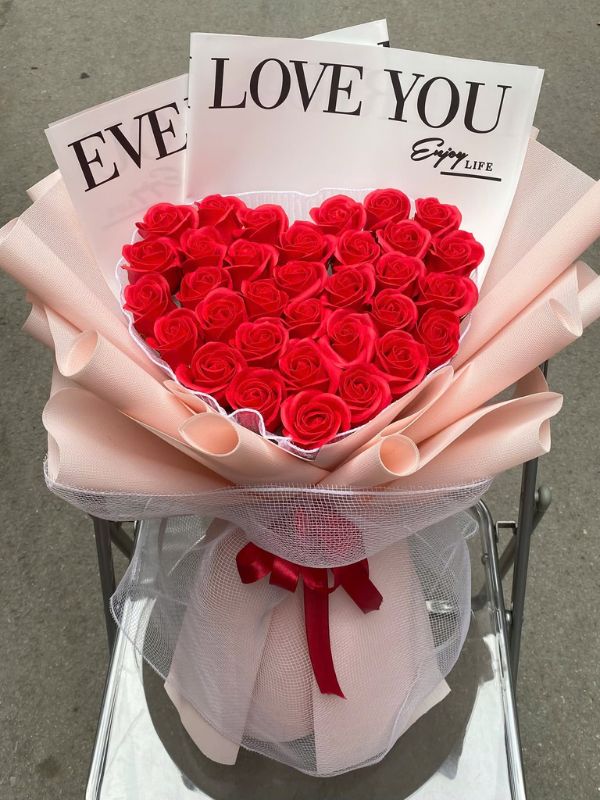 Màu sắc: đỏ. Dịp tặng: tỏ tình, cầu hôn, Valentine, kỷ niệm ngày cưới. Loại sản phẩm: Hoa sáp.

Bó Hoa Sáp Đỏ Trái Tim là mẫu trái tim cỡ lớn, sắc đỏ trải kín mặt hoa và được viền bằng voan đen xếp bèo nên nhìn nổi bật ngay từ xa. Đây là kiểu bó dành cho những dịp muốn gây ấn tượng mạnh.

Khối hoa gồm khoảng 90 đến 110 bông hồng sáp đỏ ghép sát nhau thành hình tim cân đối, mặt hoa dày và phẳng, không lộ khoảng trống.

Phần trang trí gồm dải ruy băng bản xám bạc thắt nơ chéo qua mặt tim và một dây hạt ngọc trai trắng vắt ngang, cán bó quấn ruy băng đỏ buông dài. Trái tim rộng khoảng 45 đến 55cm, cao chừng 60cm tính cả cán, cần hai tay để ôm.

Sản phẩm hợp với màn tỏ tình, cầu hôn, kỷ niệm ngày cưới hay Valentine, dành tặng người yêu, vợ, hoặc bạn gái. Chất liệu sáp giữ nguyên dáng nhiều tháng nên người nhận trưng bày được lâu.

Gọi 0934.833.013 – 0907.473.357 hoặc nhắn Facebook Hoa Mãi Mãi để đặt trước, shop nhận làm theo kích thước và màu ruy băng anh chị muốn.