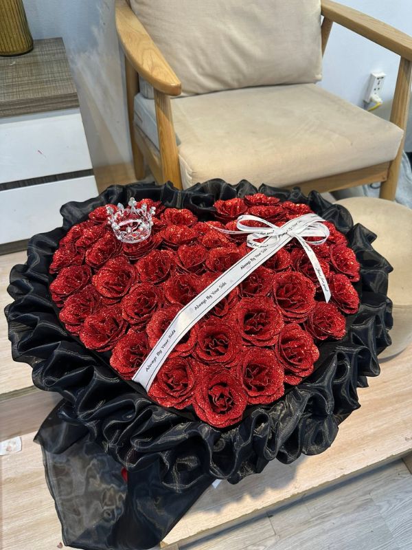 Màu sắc: đỏ ánh nhũ. Dịp tặng: tỏ tình, Valentine, kỷ niệm yêu, sinh nhật người yêu. Loại sản phẩm: Hoa sáp.

Bó Sáp Nhũ Tỏ Tình lấy sắc đỏ phủ nhũ kim tuyến làm tông màu chủ đạo, kết hợp viền voan đen trầm nên nhìn vừa rực rỡ vừa sang. Dưới ánh đèn, lớp nhũ trên cánh hồng sáp ánh lên lấp lánh, đúng chất một món quà dành cho khoảnh khắc quan trọng.

Sản phẩm kết theo dáng trái tim đầy đặn, khoảng 35 đến 45 bông hồng sáp xếp sát nhau, điểm thêm một chiếc vương miện bạc nhỏ ở góc trên.

Phần gói dùng voan lưới đen xếp bèo nhiều lớp ôm quanh viền tim, thắt nơ ruy băng bản trắng in dòng chữ "Always By Your Side". Trái tim rộng khoảng 35 đến 40cm mỗi chiều, đủ lớn để tạo bất ngờ nhưng vẫn dễ ôm, dễ chụp ảnh.

Đây là lựa chọn hợp với bạn gái, người yêu hoặc vợ trong buổi tỏ tình, lễ Valentine hay ngày kỷ niệm. Hoa sáp giữ dáng và màu rất lâu nên người nhận trưng bày được như một kỷ vật.

Gọi ngay 0934.833.013 – 0907.473.357 hoặc nhắn tin Facebook Hoa Mãi Mãi để đặt bó hoa này, shop giao tận nơi trong ngày.