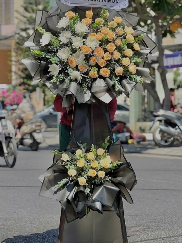 Màu sắc: trắng. Dịp tặng: lễ viếng, lễ tang, lễ nhập quan, tiễn biệt, chia buồn. Loại sản phẩm: Hoa chia buồn / hoa tang lễ.

Vòng Hoa Viếng - HCB.14 thuộc dòng kệ hoa cao cấp phúng viếng được Hoa Mãi Mãi thiết kế trang nghiêm, thường được các gia đình lựa chọn cho nghi lễ tang gia, lễ nhập quan và những giờ phút tiễn biệt đầy xúc động.

Tông màu trắng chủ đạo phối đen xuyên suốt thiết kế giúp sản phẩm toát lên khí chất trầm lắng, trang trọng, đúng tinh thần của một sản phẩm hoa chia buồn, phúng viếng.

Thành phần hoa chính gồm lan hồ điệp trắng, hồng trắng và cúc trắng, được chọn lọc kỹ càng để giữ được độ tươi lâu, phối cùng hồng môn xanh nhạt, nơ đen sang trọng nhằm tạo nên tổng thể cân đối, mềm mại mà vẫn giữ được sự trang nghiêm cần có.

Về kích thước, sản phẩm cao khoảng 1,8 – 2,0m, đường kính phần hoa chính 70 – 90cm, phù hợp đặt tại nhà tang lễ, hội trường hoặc không gian viếng có diện tích vừa và lớn; kích thước có thể điều chỉnh linh hoạt theo yêu cầu thực tế.

Thông điệp gửi viếng: có thể đính kèm dải lụa ghi tên người gửi cùng câu chia buồn quen thuộc như "Vô cùng thương tiếc", "Thành kính phân ưu" hoặc nội dung tùy chỉnh theo mong muốn gia quyến.

Tùy biến mẫu theo yêu cầu: Ngoài mẫu tiêu chuẩn, quý khách hoàn toàn có thể yêu cầu thay đổi tông màu, loại hoa hoặc kích thước cho phù hợp với hoàn cảnh cụ thể; Hoa Mãi Mãi cam kết hoa luôn tươi mới và giao hàng tận nơi đúng hẹn.