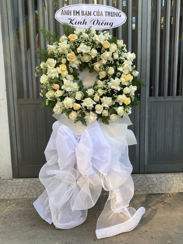 Màu sắc: của sản phẩm là trắng tinh khôi. Dịp tặng: lễ viếng, lễ tang, lễ nhập quan, tiễn biệt, chia buồn. Loại sản phẩm: Hoa chia buồn / hoa tang lễ.

Vòng Hoa Đám Tang - HCB.13 là mẫu kệ hoa hình trăng khuyết tang lễ được các nghệ nhân Hoa Mãi Mãi chăm chút tỉ mỉ từng chi tiết, phù hợp sử dụng trong lễ viếng, lễ truy điệu, lễ động quan hay giờ phút tiễn đưa người đã khuất về nơi an nghỉ cuối cùng.

Tone màu chủ đạo của sản phẩm là trắng tinh khôi, được phối hợp hài hòa để toát lên vẻ trang nghiêm, thanh khiết, phù hợp với không khí lặng lẽ, tiếc thương của tang lễ.

Hoa chính được sử dụng là hồng trắng, cúc tana trắng nhỏ và lan hồ điệp trắng, loại hoa tượng trưng cho sự thanh khiết, kết hợp khéo léo cùng hồng môn trắng, nơ trắng đen để hoàn thiện bố cục cân xứng, giàu cảm xúc.

Sản phẩm có kích thước cao khoảng 1,6 – 1,7m, đường kính phần hoa chính 60 – 70cm, vừa đủ nổi bật khi đặt cạnh các sản phẩm hoa khác mà vẫn giữ được sự trang trọng; kích thước có thể tùy chỉnh theo yêu cầu riêng.

Thông điệp gửi viếng: kèm theo băng rôn chia buồn được viết trang trọng, thể hiện tấm lòng thành kính qua các cụm từ quen thuộc như "Thành kính phân ưu", "Vô cùng thương tiếc" hoặc nội dung riêng theo yêu cầu.

Tùy biến mẫu theo yêu cầu: Mọi yêu cầu tùy chỉnh về màu sắc, loại hoa, kích thước hay thông điệp đi kèm đều được Hoa Mãi Mãi tiếp nhận và thực hiện chu đáo, đảm bảo giao hoa tận nơi nhanh chóng, hoa tươi ngay trong ngày lễ tang.
