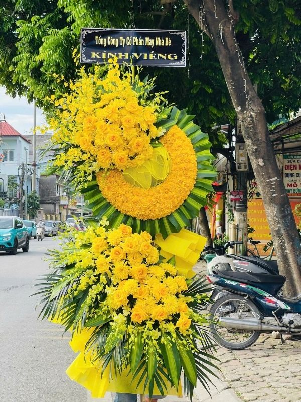 Màu sắc: đỏ. Dịp tặng: lễ viếng, lễ tang, lễ nhập quan, tiễn biệt, chia buồn. Loại sản phẩm: Hoa chia buồn / hoa tang lễ.

Lẵng Hoa Viếng Đám Tang - HCB.59 là kệ hoa tang lễ mang phong cách trang trọng, cổ điển, do đội ngũ Hoa Mãi Mãi thực hiện thủ công tỉ mỉ, phù hợp đặt tại tang gia, nhà tang lễ hoặc nghĩa trang trong suốt quá trình lễ tang.

Tông màu vàng rực rỡ xuyên suốt thiết kế giúp sản phẩm toát lên khí chất trầm lắng, trang trọng, đúng tinh thần của một sản phẩm hoa chia buồn, phúng viếng.

Thành phần hoa chính gồm hồng vàng và lan mokara vàng, được chọn lọc kỹ càng để giữ được độ tươi lâu, phối cùng lá cau xanh nhằm tạo nên tổng thể cân đối, mềm mại mà vẫn giữ được sự trang nghiêm cần có.

Về kích thước, sản phẩm cao khoảng 1,8 – 2,0m, đường kính phần hoa chính 70 – 90cm, phù hợp đặt tại nhà tang lễ, hội trường hoặc không gian viếng có diện tích vừa và lớn; kích thước có thể điều chỉnh linh hoạt theo yêu cầu thực tế.

Thông điệp gửi viếng: đi kèm bảng chữ chia buồn trang nghiêm, có thể ghi "Thành kính phân ưu", "Vô cùng thương tiếc" hay lời tiễn biệt riêng theo mong muốn của người gửi.

Tùy biến mẫu theo yêu cầu: Mọi yêu cầu tùy chỉnh về màu sắc, loại hoa, kích thước hay thông điệp đi kèm đều được Hoa Mãi Mãi tiếp nhận và thực hiện chu đáo, đảm bảo giao hoa tận nơi nhanh chóng, hoa tươi ngay trong ngày lễ tang.