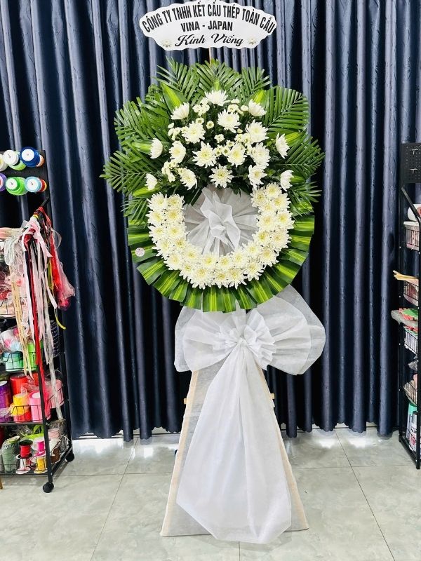 Màu sắc: trắng tím nhẹ nhàng. Dịp tặng: lễ viếng, lễ tang, lễ nhập quan, tiễn biệt, chia buồn. Loại sản phẩm: Hoa chia buồn / hoa tang lễ.

Lời Tạm Biệt - HCB.01 là kệ hoa hình tam giác tang lễ mang phong cách trang trọng, cổ điển, do đội ngũ Hoa Mãi Mãi thực hiện thủ công tỉ mỉ, phù hợp đặt tại tang gia, nhà tang lễ hoặc nghĩa trang trong suốt quá trình lễ tang.

Bảng màu trắng tím nhẹ nhàng chủ đạo mang đến sự cân bằng giữa nỗi buồn tiễn biệt và sự ấm áp, chân thành, giúp người gửi truyền tải trọn vẹn tấm lòng của mình.

Thành phần hoa chính gồm hồng trắng và hồng môn xanh, được chọn lọc kỹ càng để giữ được độ tươi lâu, phối cùng lan mokara tím nhẹ, lá cau nhằm tạo nên tổng thể cân đối, mềm mại mà vẫn giữ được sự trang nghiêm cần có.

Về kích thước, sản phẩm cao khoảng 1,6 – 1,7m, đường kính phần hoa chính 60 – 70cm, phù hợp đặt tại nhà tang lễ, hội trường hoặc không gian viếng có diện tích vừa và lớn; kích thước có thể điều chỉnh linh hoạt theo yêu cầu thực tế.

Thông điệp gửi viếng: kèm dải băng tang trang trọng ghi rõ tên người hoặc đơn vị gửi viếng cùng lời chia buồn như "Thành kính phân ưu", "Vô cùng thương tiếc" hoặc "Kính viếng" theo nội dung quý khách yêu cầu.

Tùy biến mẫu theo yêu cầu: Hoa Mãi Mãi nhận đặt hoa theo yêu cầu riêng về màu sắc, chất liệu hoa và kích thước, đảm bảo mỗi sản phẩm đều được thực hiện tỉ mỉ, giao đến tận nơi nhanh chóng và đúng thời gian tổ chức lễ tang.