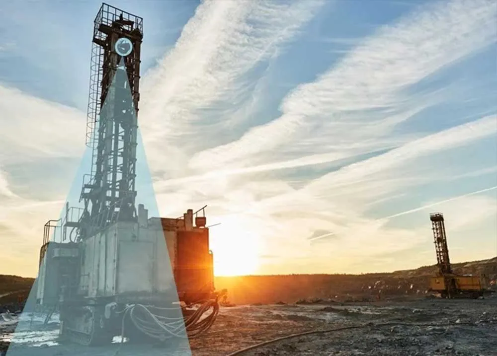 Mining site at sunset with two large drill machines on rocky ground under a cloudy sky.