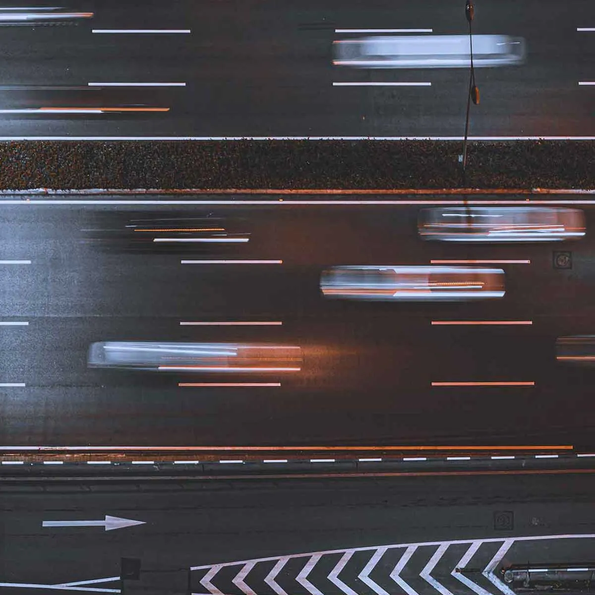 Aerial night view of a highway with cars blurred by motion and road lane markings visible.