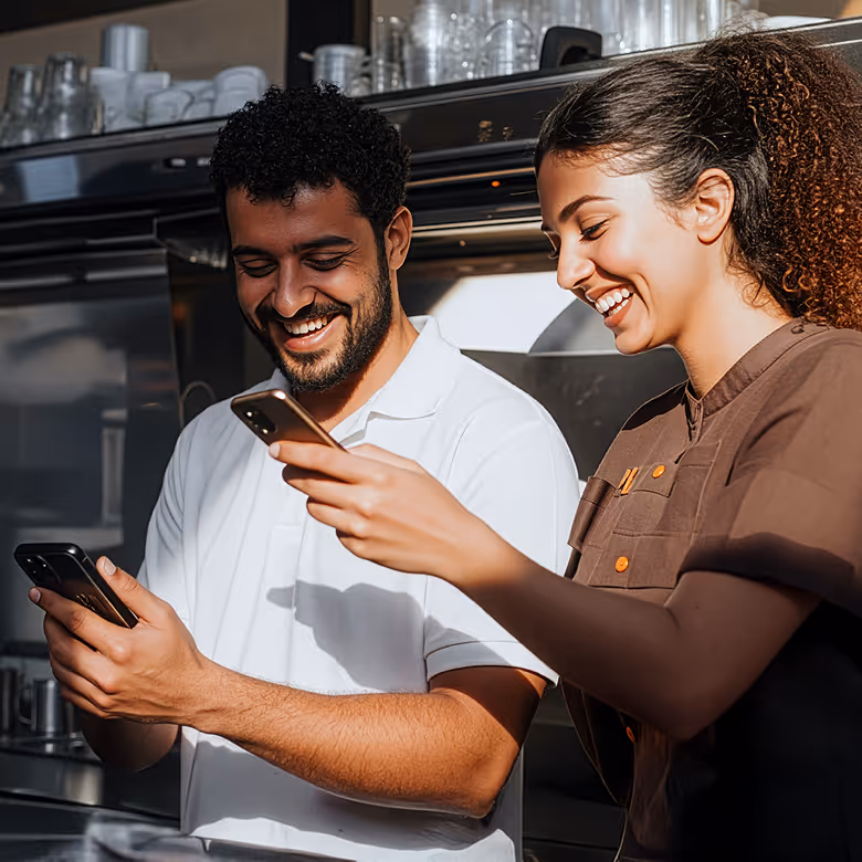 Un homme et une femme souriants regardent leurs téléphones ensemble dans une cuisine professionnelle.