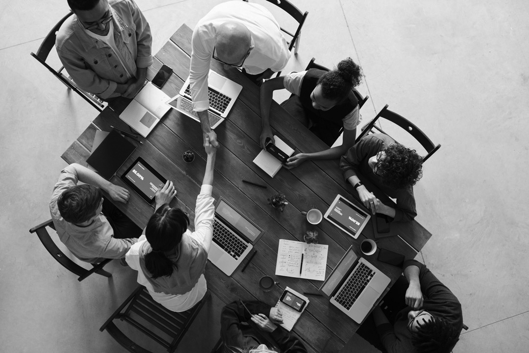 group of diverse people working around a table with laptops and tablets black and white