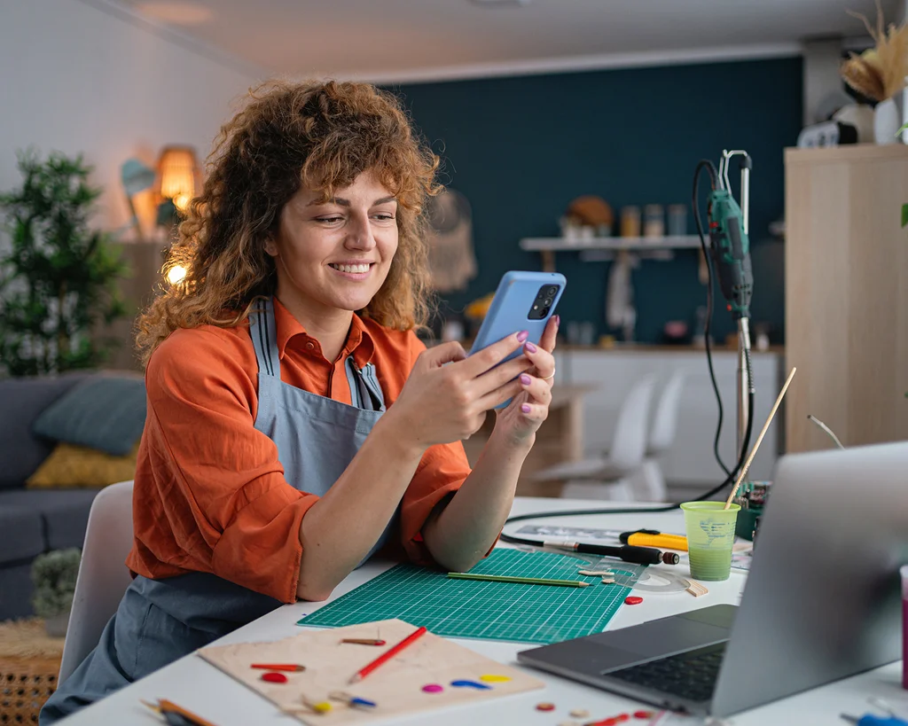 Provider looking at smartphone while sitting at a desk full of art supplies