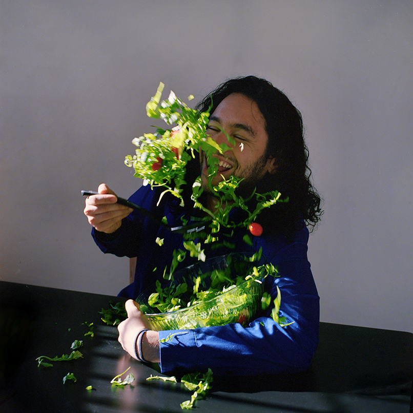 renan joyfully tossing a salad with arugula and cherry tomatoes. He is laughing.